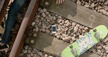 Young person laying on tracks with mobile and skateboard